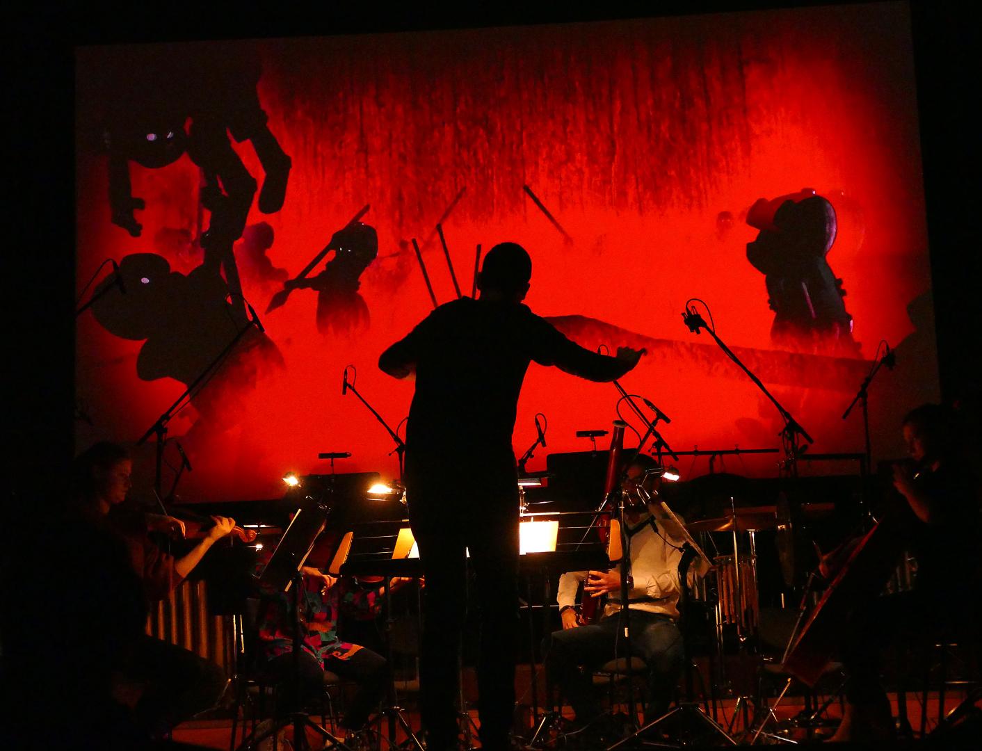 Ein Dirigent leitet ein Orchester mit Livemusik zu einem Stummfilm