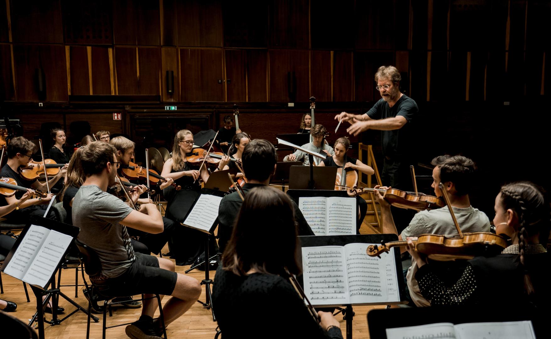 Probe des Collegium Musicum (Orchester der Lehramtsstudierenden), Musiker*innen und Dirigent auf der Bühne.