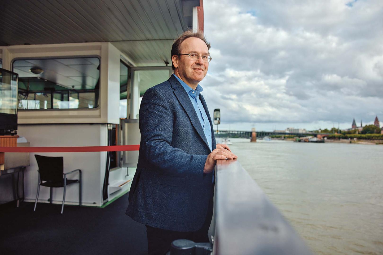 Klement Tockner steht auf einem Schiff an der Reeling und blickt an der Kamera vorbei auf den Fluss.