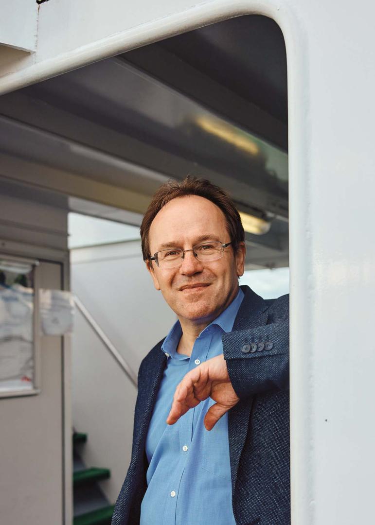 Porträt von Klement Tockner, er lehnt auf einem Schiff mit dem linken Ellenbogen an einer Wand und blickt in die Kamera.