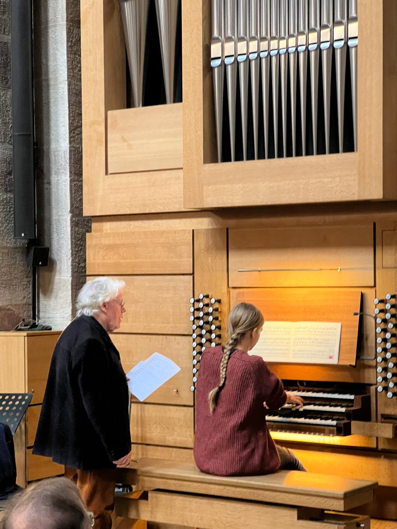 Studentin sitzt an der Orgel, Daniel Roth steht daneben und erklärt etwas