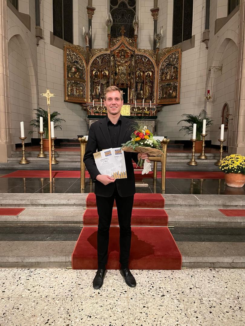 Manuel Pschorn im Anzug in einer Kirche mit Blumenstrauß und zwei Urkunden in den Händen