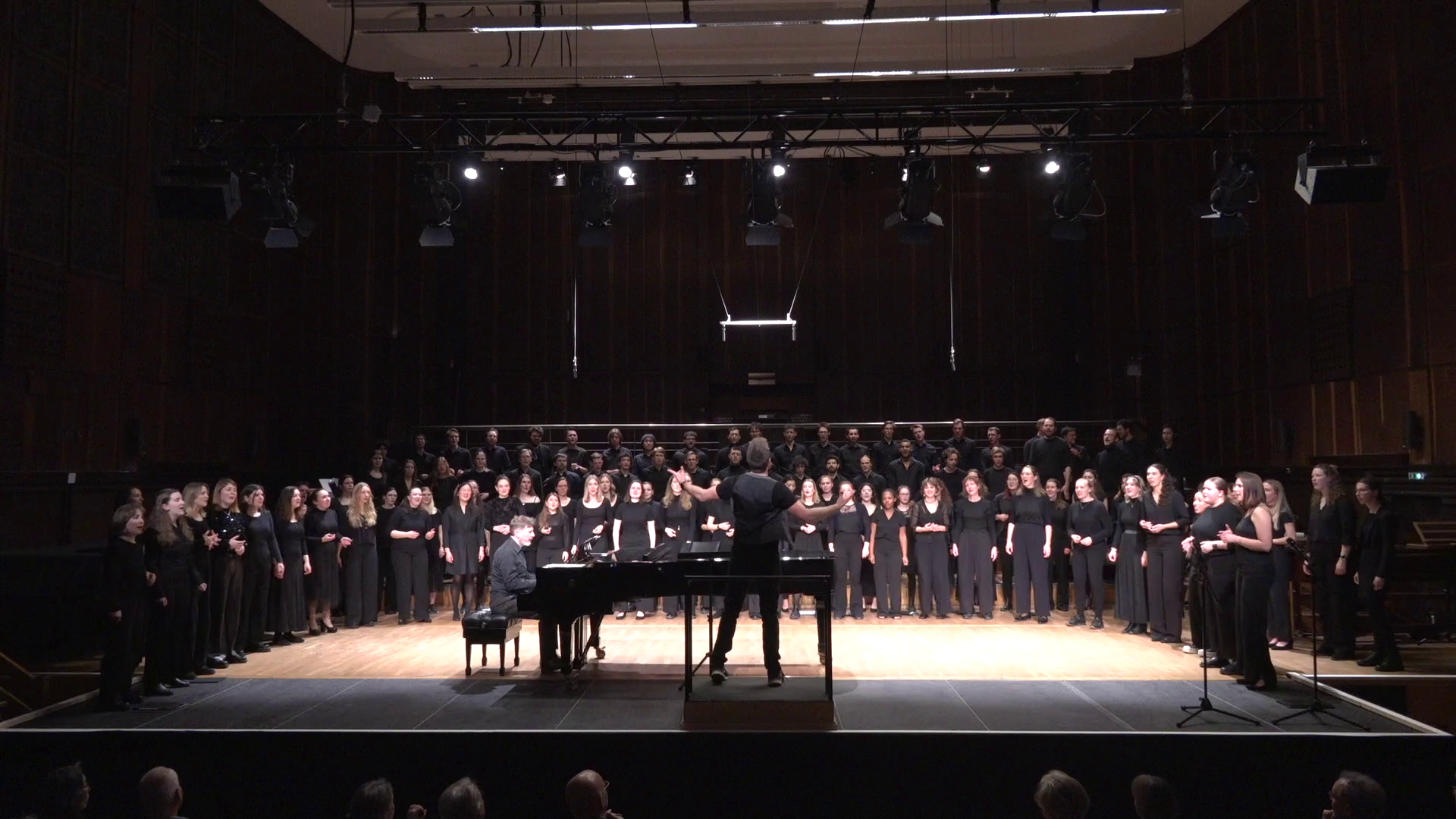 Frontalansicht: Fabian Sennholz dirigiert großen Chor, Ralph Abelein spielt am Flügel