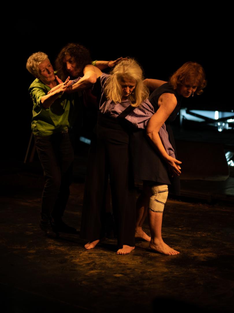 Vier Frauen stehen eng beieinander auf einer Bühne und bewegen sich mit kleinen Tanzbewegungen auf einer Bühne zueinander..
