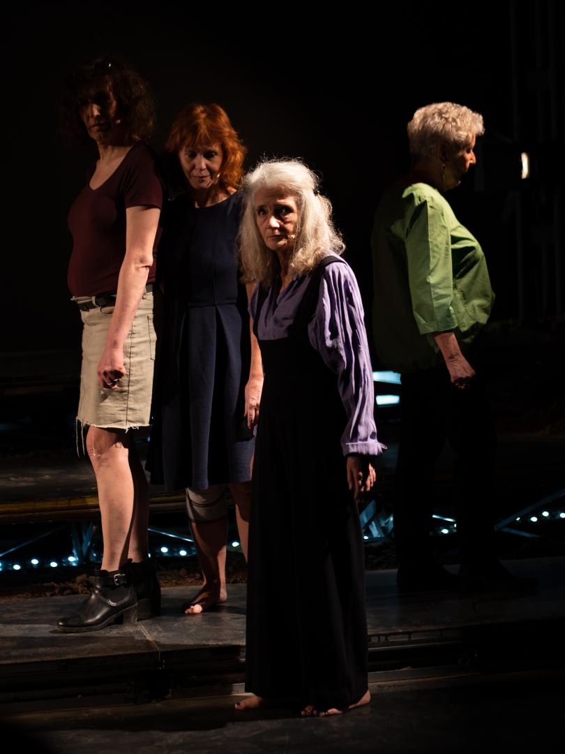 Vier Frauengestalten sind im Ganzkörper auf einer Bühne stehend zu sehen. Eine Frau am linken Rand und zwei Frauen in der Mitte blicken nach vorn, die vierte Frau am rechten Rand blickt nach rechts außen.