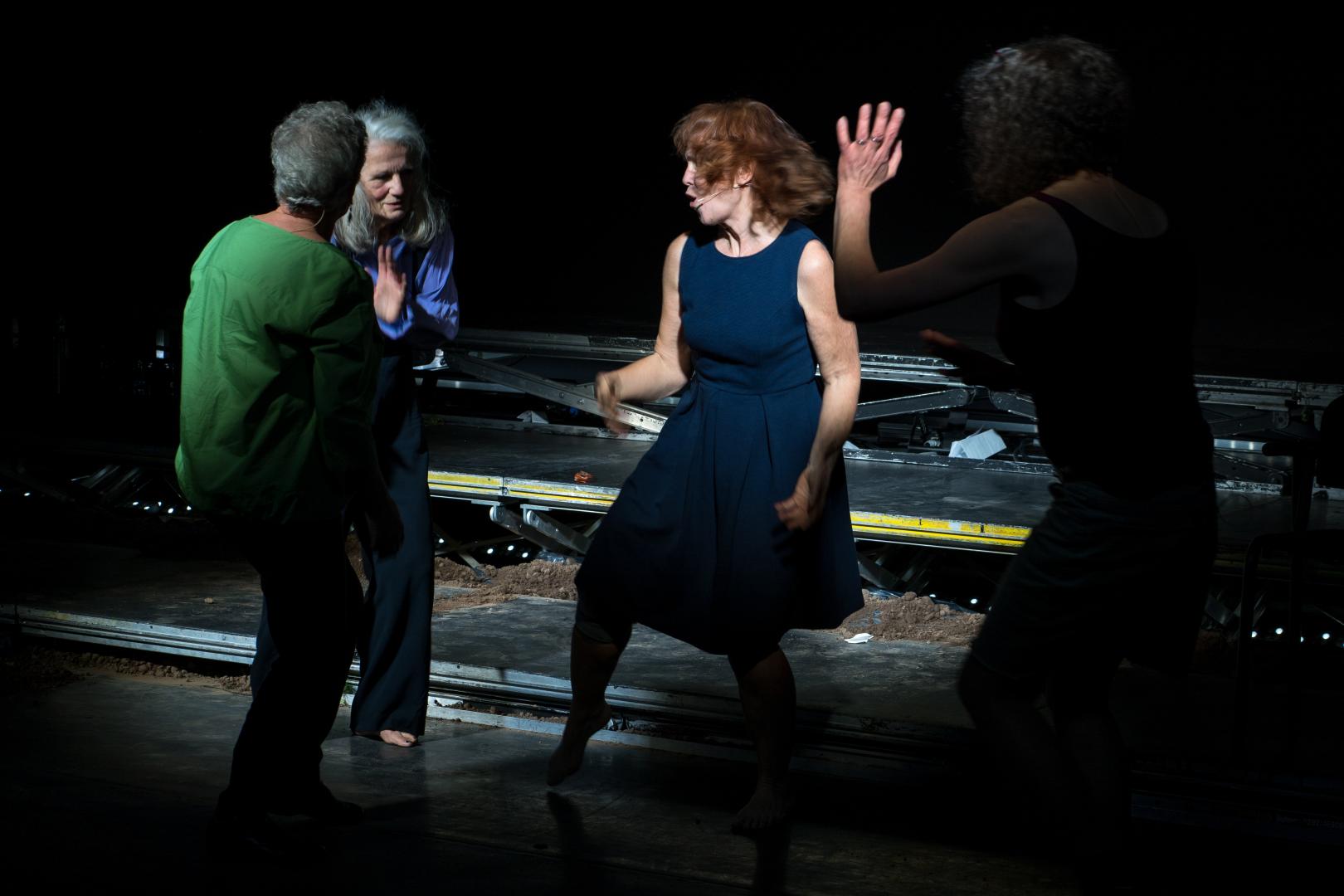 Vier Frauen stehen gestikulierend und mit kleinen Tanzbewegungen auf einer Bühne.