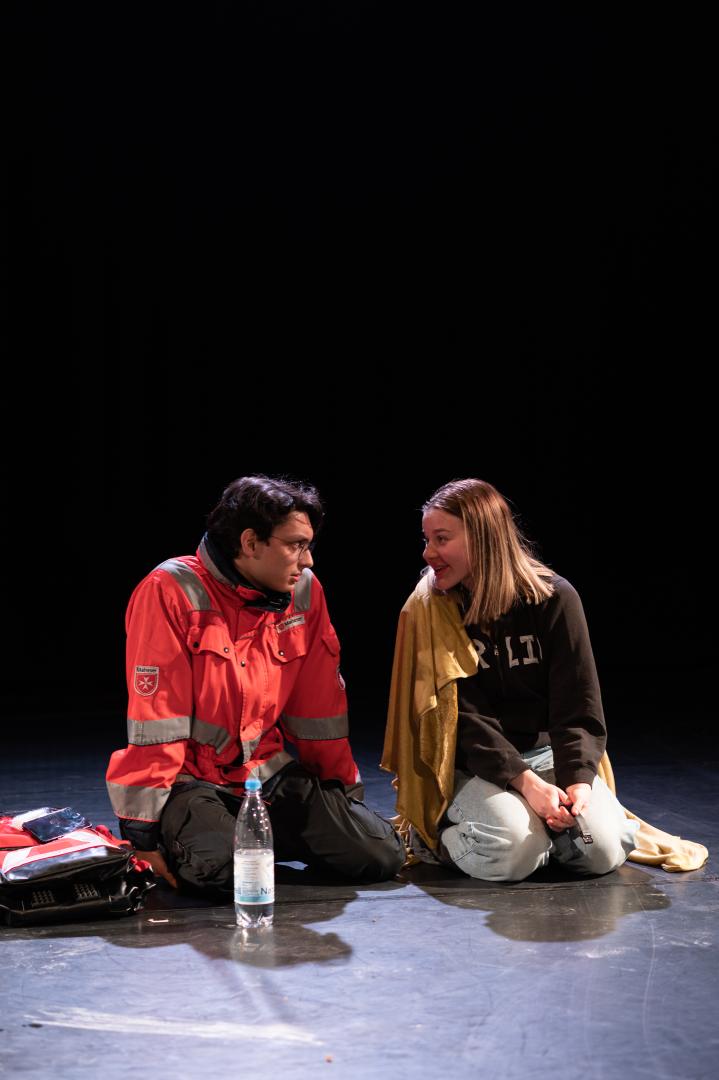 Ein Sanitäter sitzt neben einer jungen Frau auf dem Boden.
