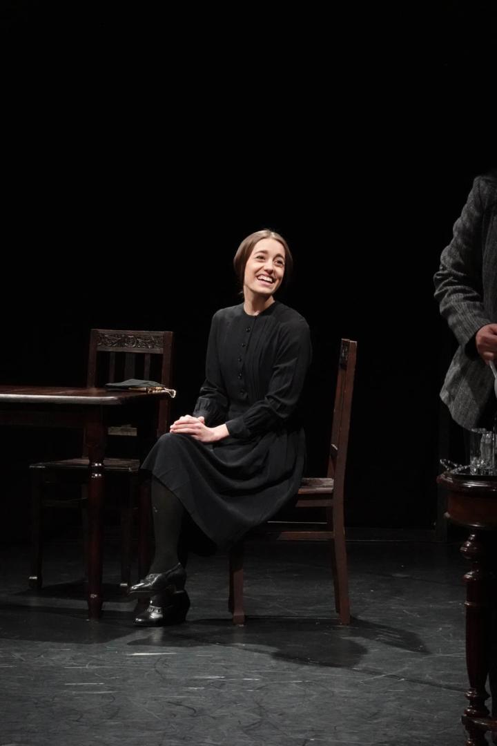 Eine Frau in dunkler Kleidung sitzt lächelnd auf einem Stuhl.