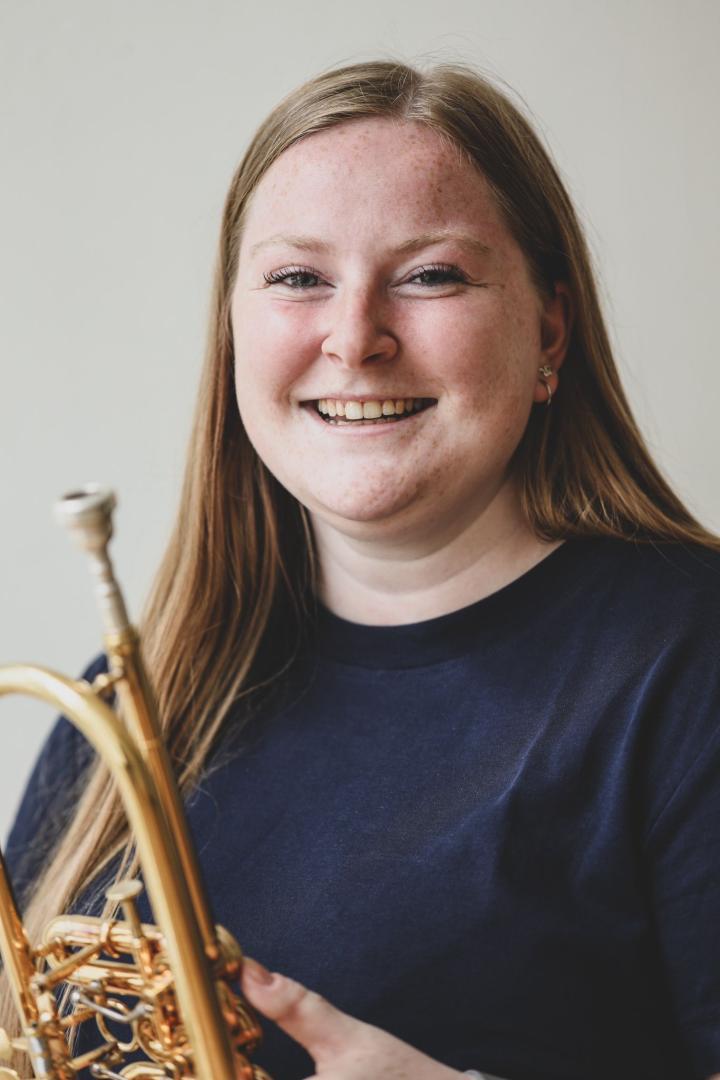 Ein Portraitfoto von Lisa Schiffler: Sie hält ihre Trompete in der Hand und lacht in die Kamera.