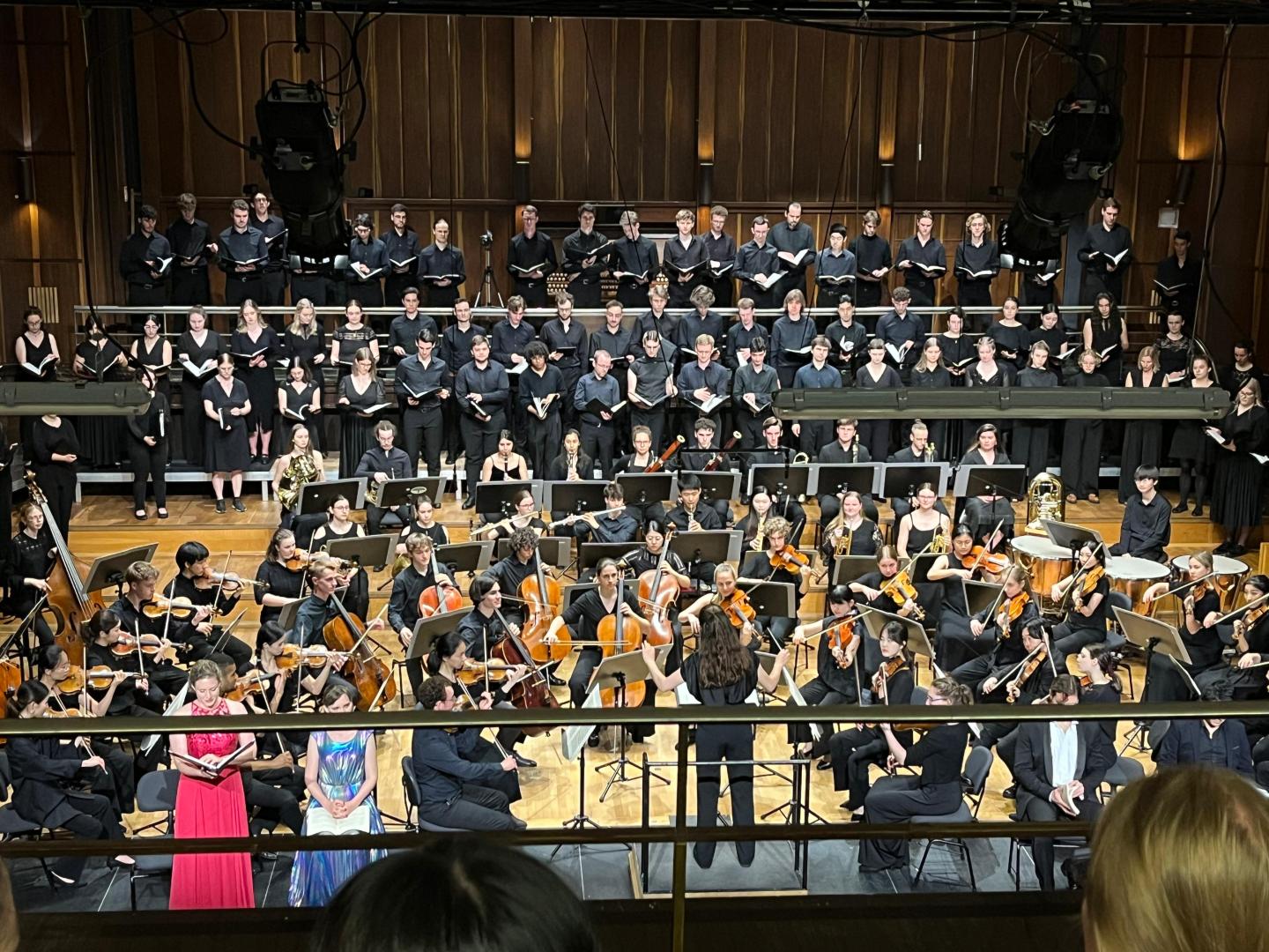 Blick auf Bühne im großen Saal, eine Studentin dirigiert Chor und Orchester