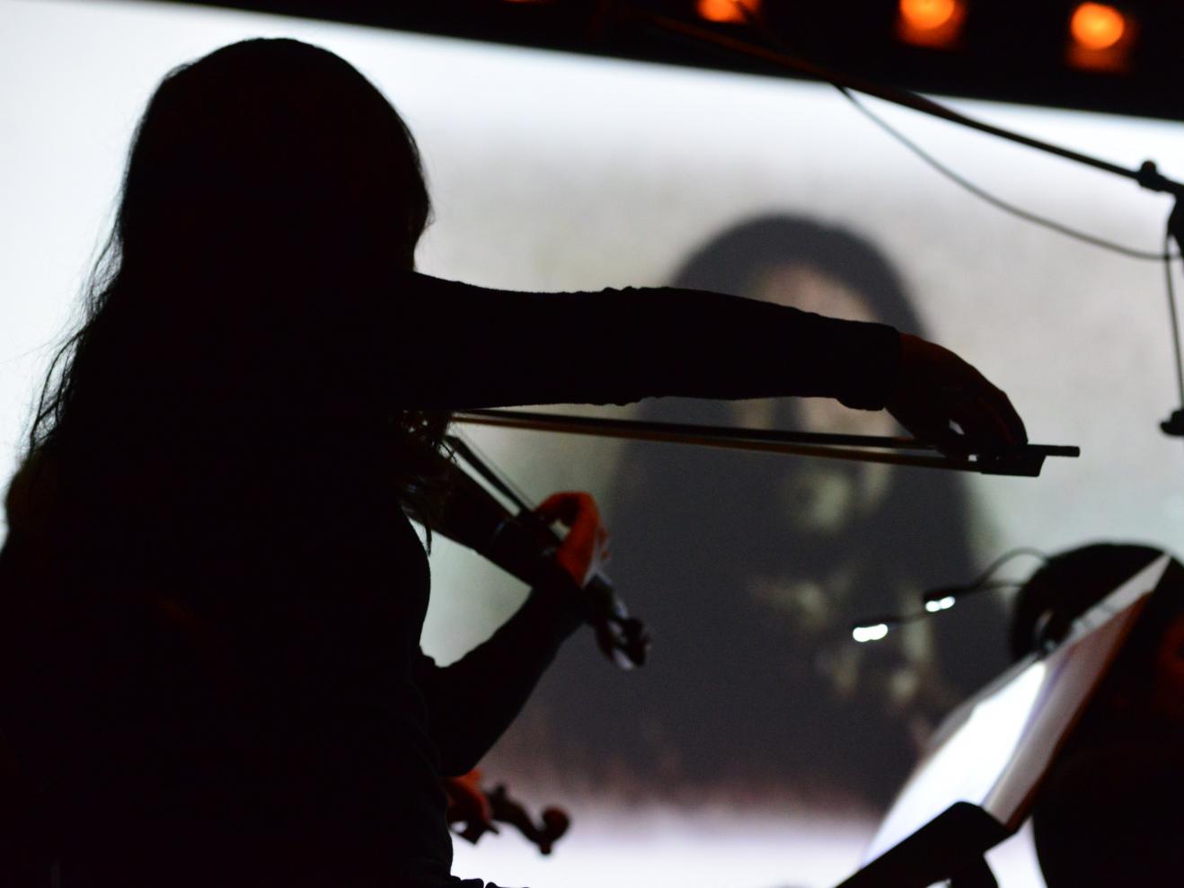 musizierende Streicherin (Rückenansicht) vor Filmleinwand