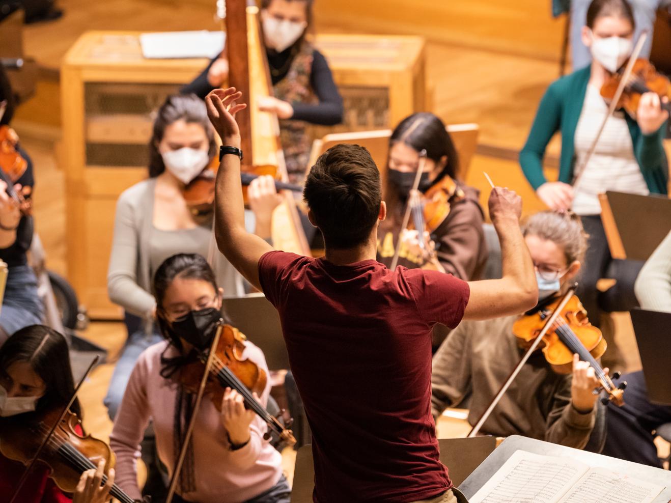 Dirigierstudent leitet ein Orchester, Hand und Taktstock erhoben.