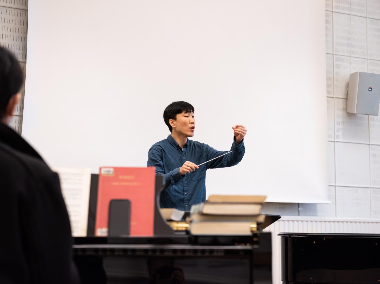 Dirigierstudent im Unterricht an der HfMDK Frankfurt, im Vordergrund ein Pianist am Klavier.