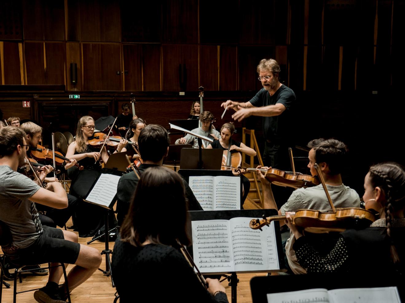 Probe des Collegium Musicum (Orchester der Lehramtsstudierenden), Musiker*innen und Dirigent auf der Bühne.