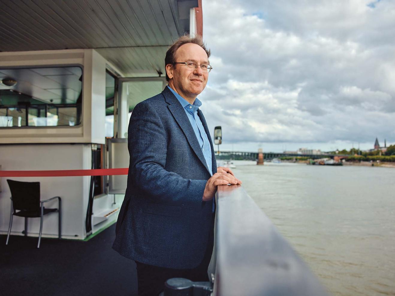 Klement Tockner steht auf einem Schiff an der Reeling und blickt an der Kamera vorbei auf den Fluss.