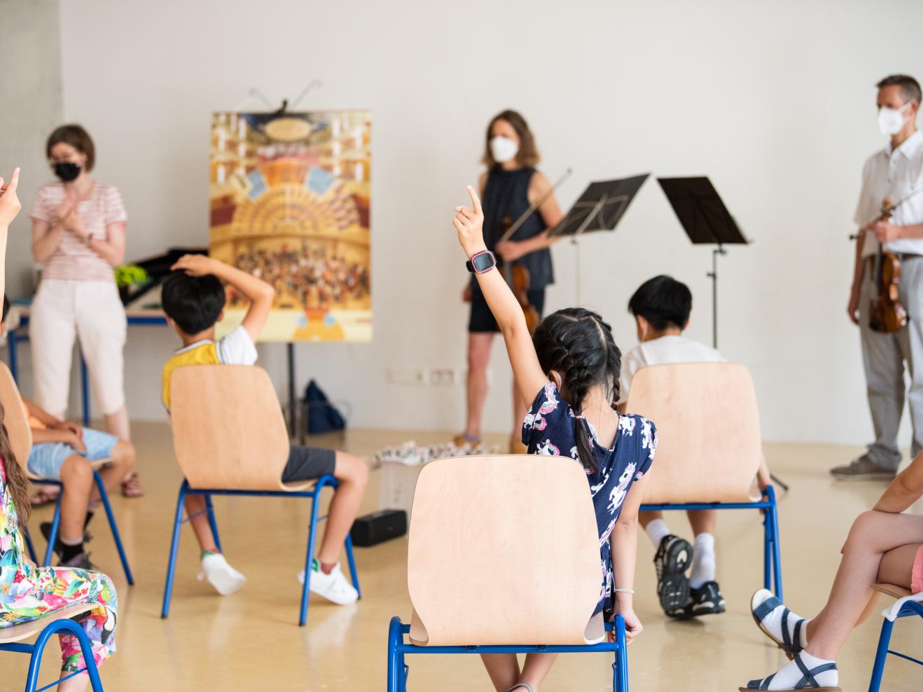 Musikprojekt mit einer Schulklasse, zwei Schülerinnen melden sich, sie sind im Vordergrund von hinten zu sehen.