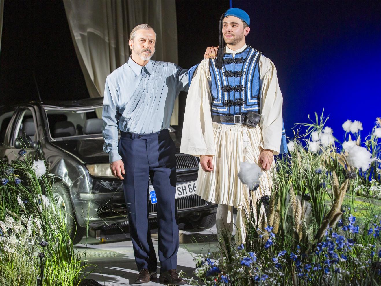 Zwei Männer vor einem Auto inmitten von Gras und Blumen.